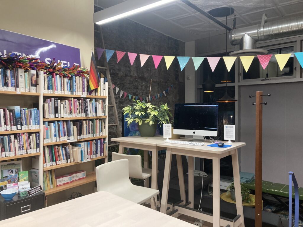 Image of Out on the Shelf space, computer and books with pride flag