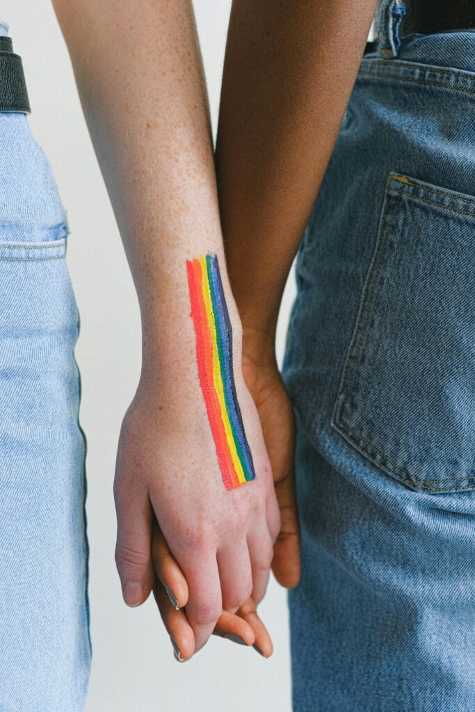 A close-up of an interracial couple holding hands with a rainbow drawn on the wrist, symbolizing LGBTQ pride.